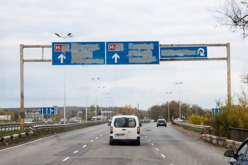 Van driving down an empty highway. The road signs have been painted over.