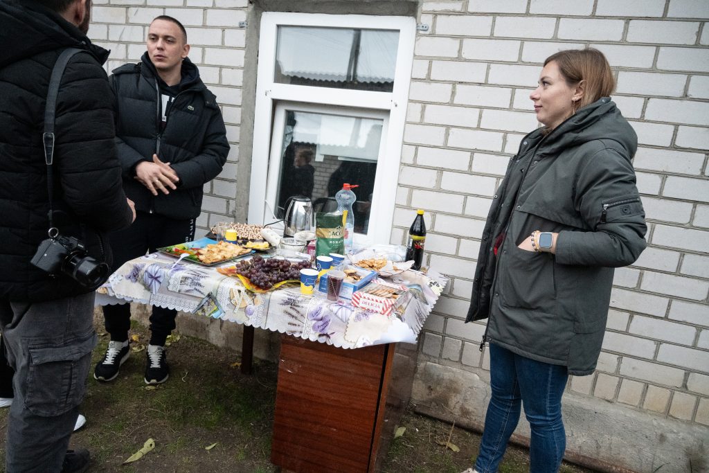 Two people stand by a small table covered in snacks and refreshments.