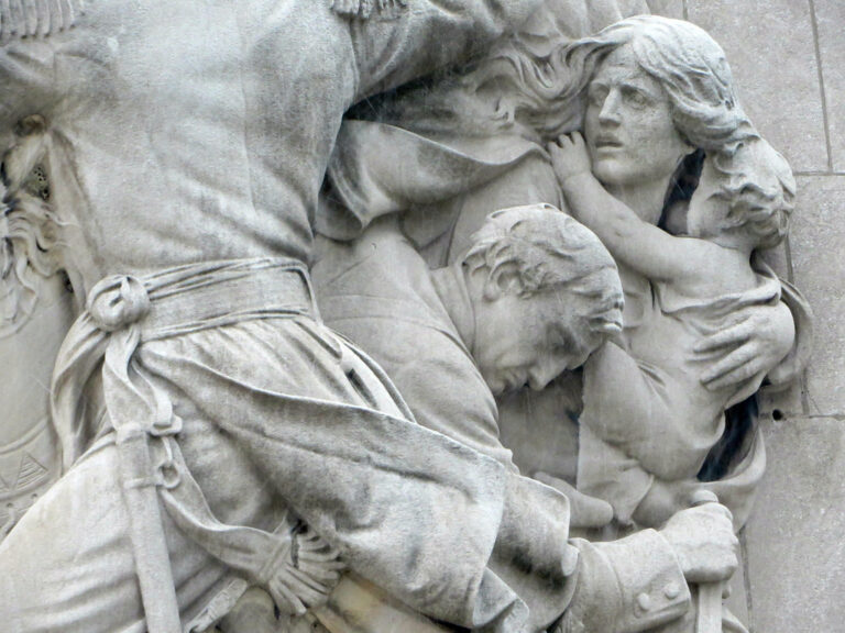 White (perhaps marble) statue showing a man, woman, and child cowering as another figure marches past.