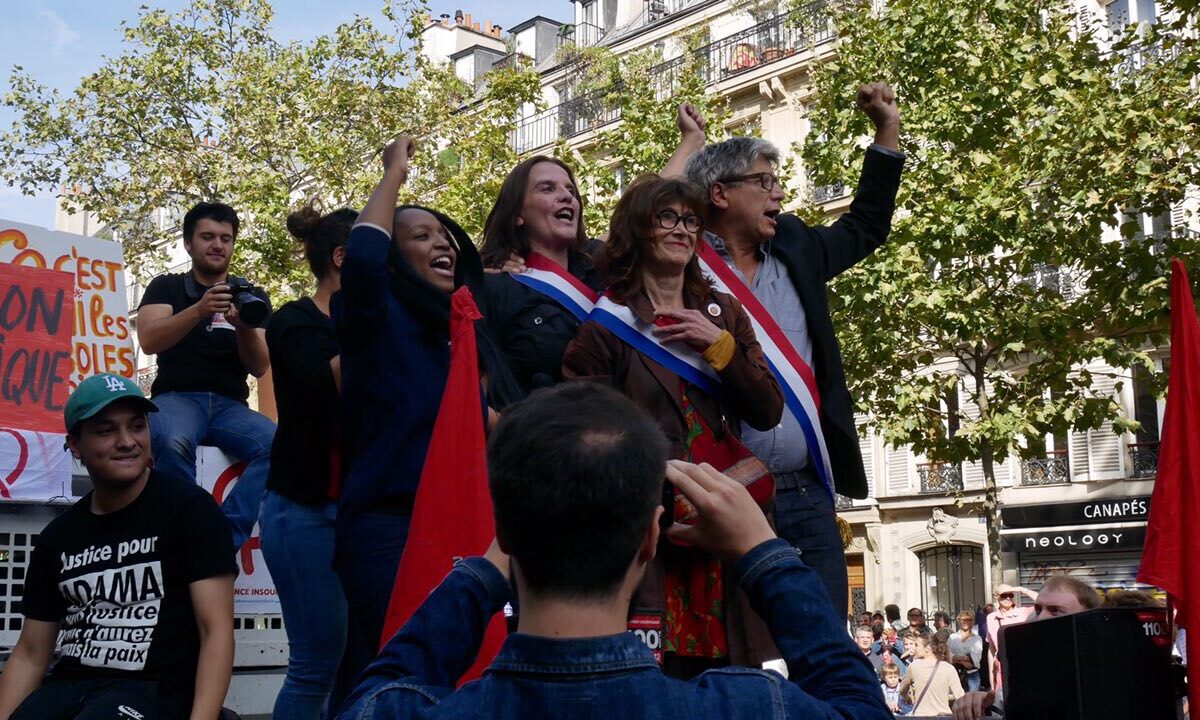 Members of the France Insoumise party on a float during a parade. Some are triumphantly raising fists.