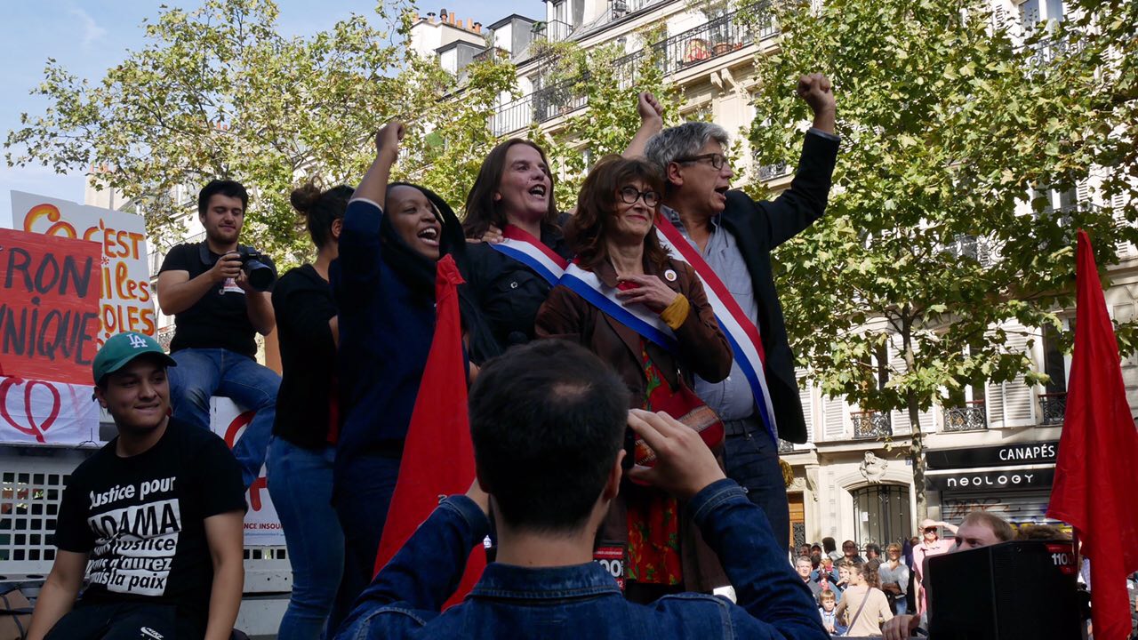 Members of the France Insoumise party on a float during a parade. Some are triumphantly raising fists.