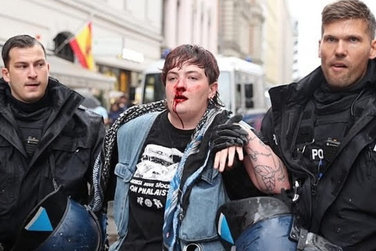 Kitty O'Brien with a bloody nose, being led away by two police officers.