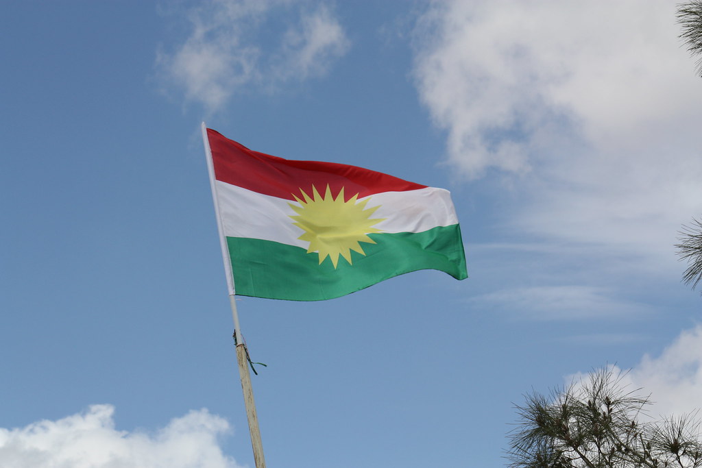 A Kurdish flag in front of a blue sky.