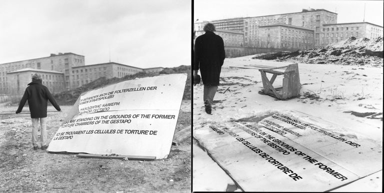 Two black and white images side by side. On the left, a figure stands with their back to the camera next to a partially broken sign which has been propped up on something. The figure has their arms slightly raised. A pile of rubble and some blocky buildings stand in the background. On the right, the same figure walks away from the camera, hands in pockets. The sign is flat on the ground. The sign displays the same sentence in various languages: "You are standing on the grounds of the former torture chamber of the Gestapo."